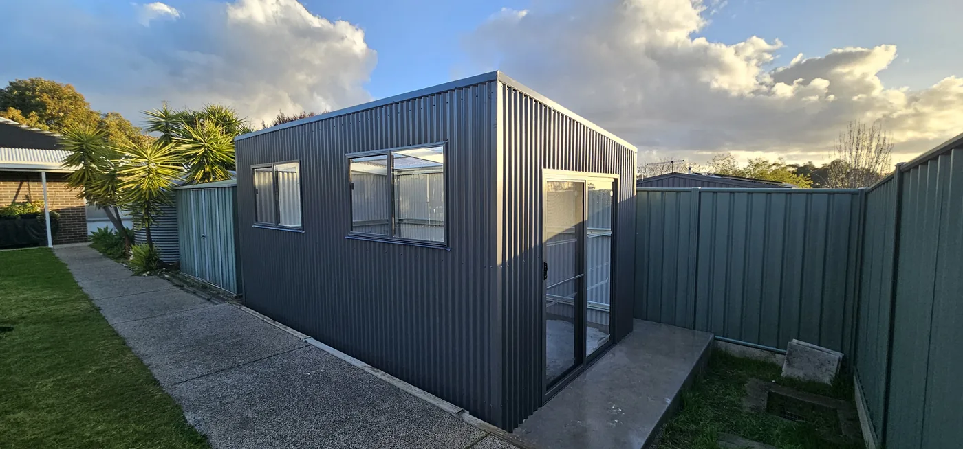 A backyard studio clad in dark steel with a glass sliding door, at dusk